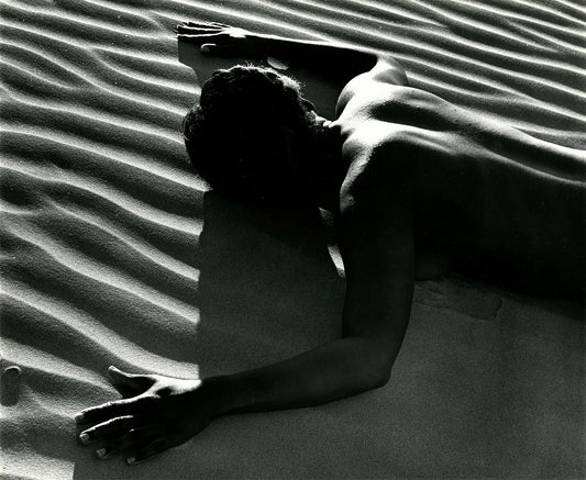 An unframed black and white print titled ‘Classic Nude and Dune’ by Brett Weston that capture a male nude figure gracefully laying on sand dunes, forming mesmerising optical patterns