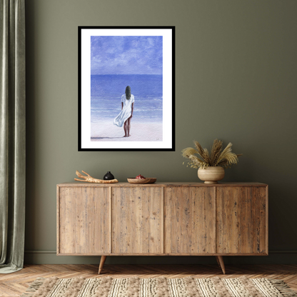"Girl on Beach, 1995" by Lincoln Seligman. This captivating black framed print depicts a woman in a flowing white dress standing on the pristine sands, gazing towards the azure waters. Bring the tranquillity of the seaside into your space with this archival digital print on Hahnemühle German etching paper.