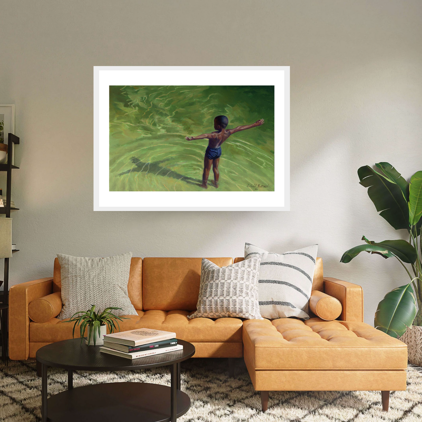 White framed print ‘Me’ by Colin Bootman is a vibrant contemporary landscape where a boy wearing a swimming suit is seen from above, standing with open arms in a bright green river water 