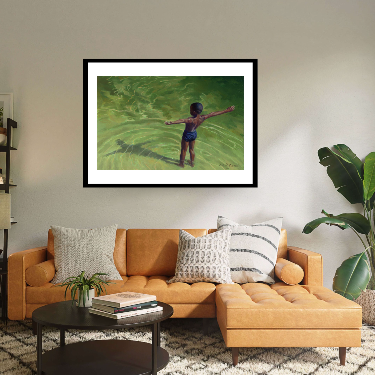 Set in an elegant interior the black framed print ‘Me’ by Colin Bootman is a vibrant contemporary landscape where a boy wearing a swimming suit is seen from above, standing with open arms in a bright green river water 