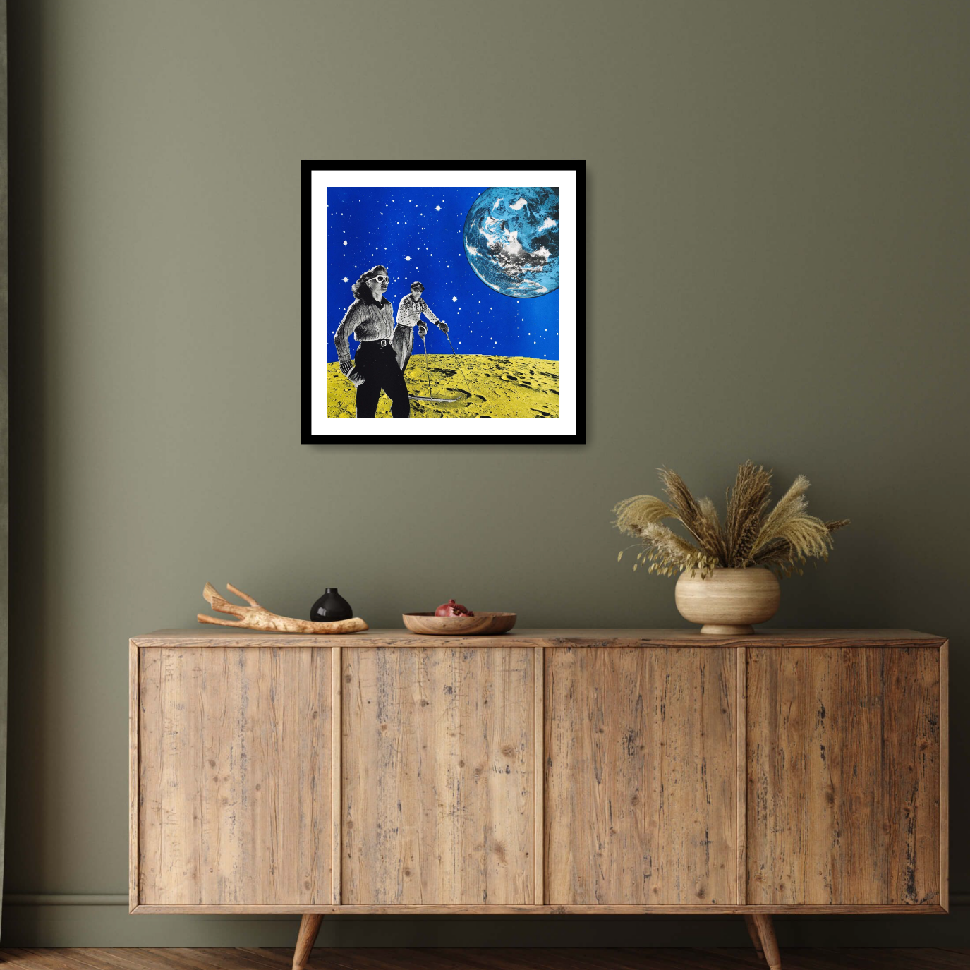 Image of the black framed print ‘Hiking space' by Anne Storno, depicting a man and a woman in chic outfits ski upon the surface of a vibrant yellow moon; A light blue and white coloured Earth floats in the background, against a sky full of sparkling stars