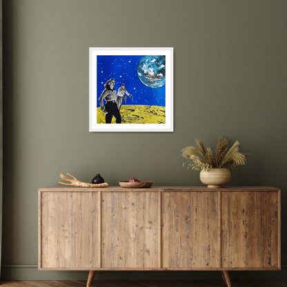 Image of the white framed print ‘Hiking space' by Anne Storno, depicting a man and a woman in chic outfits ski upon the surface of a vibrant yellow moon; A light blue and white coloured Earth floats in the background, against a sky full of sparkling stars