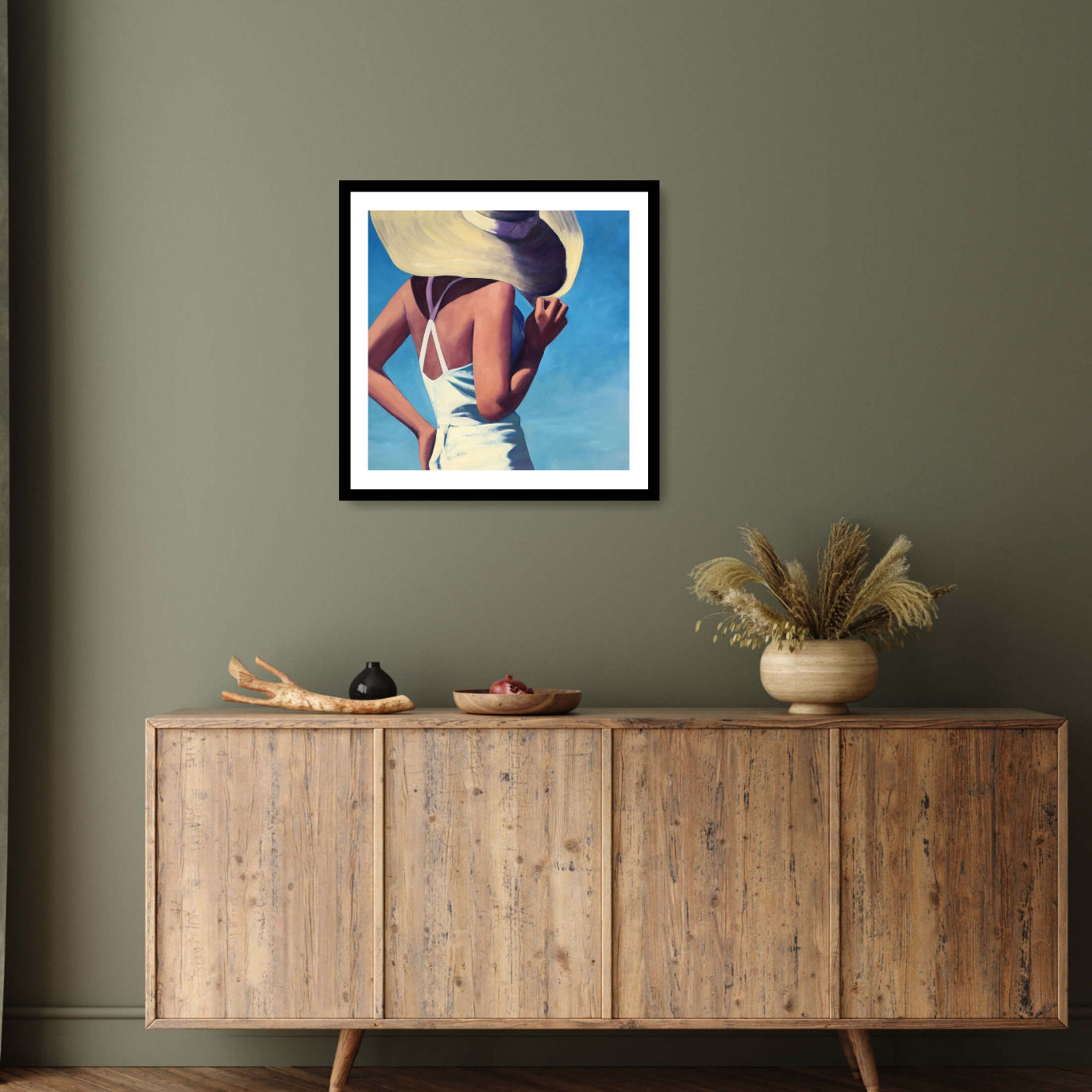 "Sunlight" by T.S. Harris beautifully blends nostalgia with vibrant hues, depicting a woman in white against a serene blue backdrop. One hand rests on her hip while the other adjusts her sunhat. Hangs framed in black elegant interior.